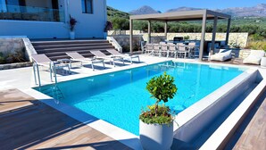 Une piscine avec des chaises longues, un espace de détente couvert et une vue sur les montagnes.