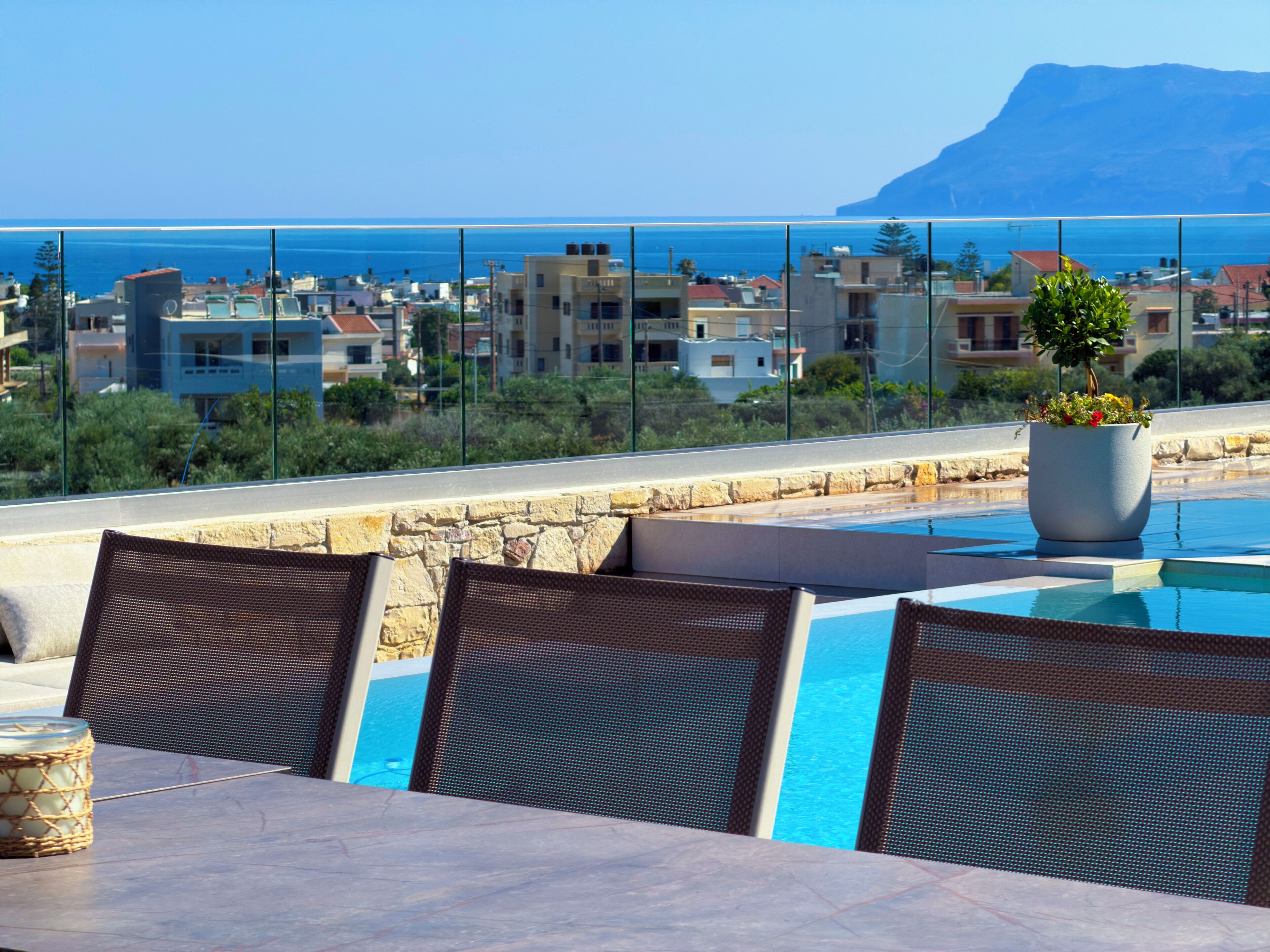 Zona junto a la piscina con sillas, una mesa, una planta en maceta y vistas a edificios y una montaña.