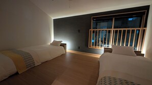 Ein Hotelzimmer mit zwei Betten, einem großen Fenster mit Jalousien und einer dunklen Wand.
