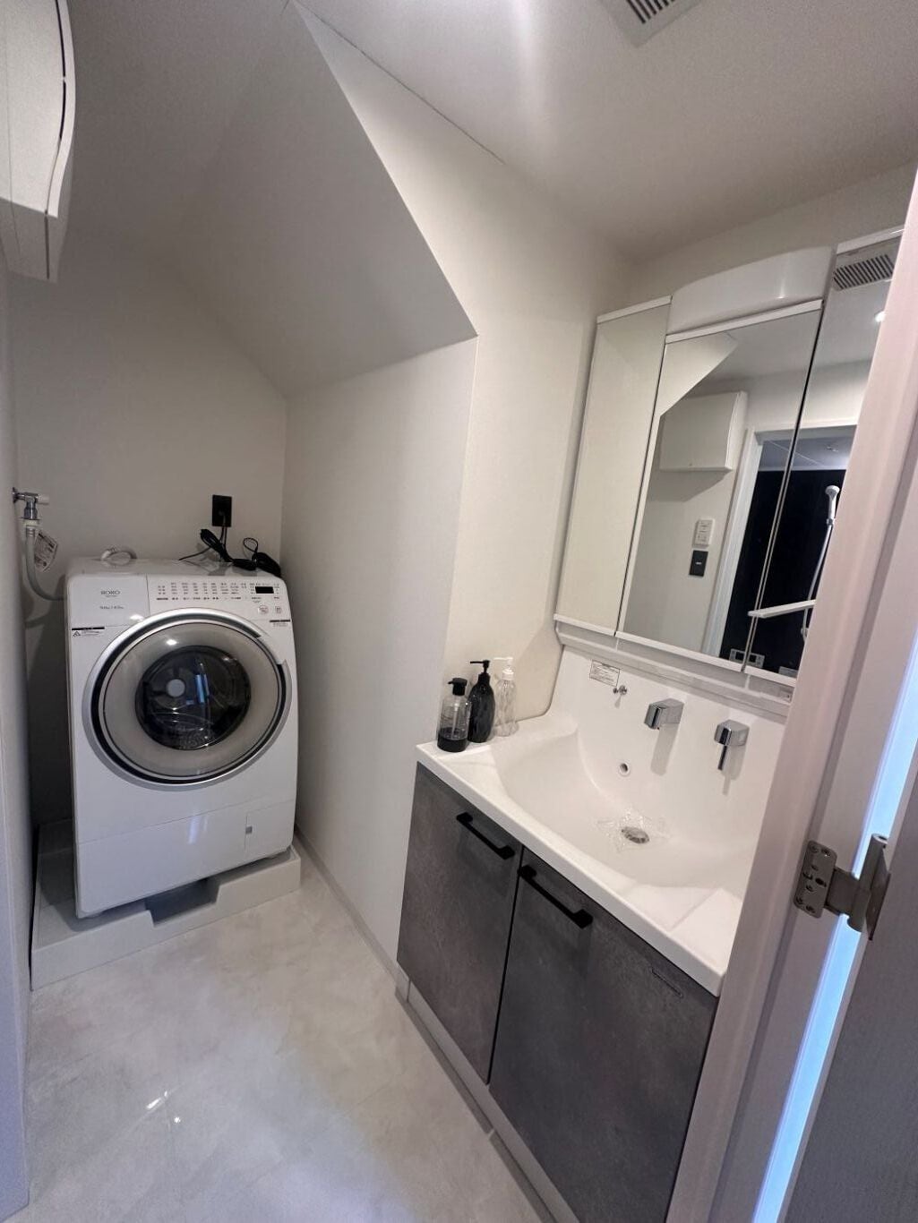 Une petite salle de bain équipée d’un lave-linge, d’un lavabo et d’un miroir.
