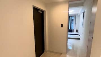 A hallway with a door, a light fixture, and a glimpse of a bed in the distance.