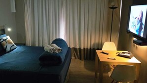 Hotellihuone, jossa on sänky, työpöytä, tuoli, televisio ja verhot.