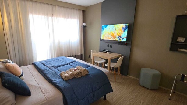 Hotellihuone, jossa on sänky, työpöytä, televisio ja pyörätuoli.
