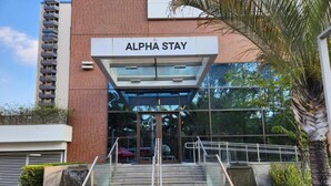 Hotellin sisäänkäynti, jossa on kyltti, jossa lukee ”ALPHA STAY”, lasinen julkisivu ja portaat, jotka johtavat sisäänkäynnille.