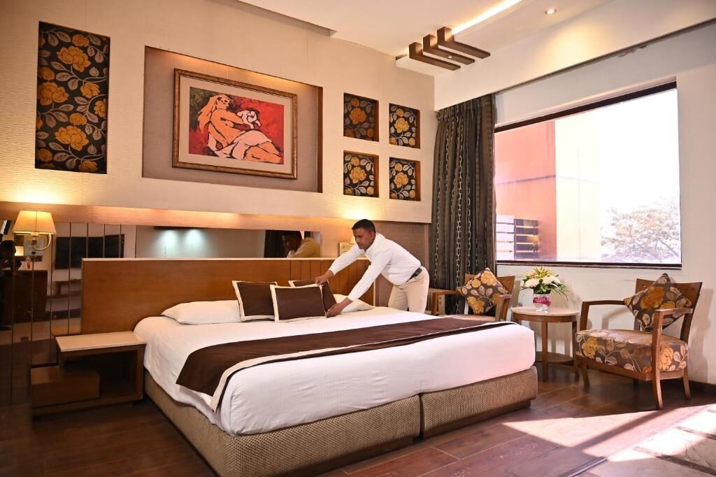 Une chambre d’hôtel avec un grand lit, un coin salon, des œuvres d’art accrochées aux murs et une vue par la fenêtre.