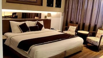 A hotel room with a large bed, a desk, a chair, a painting on the wall, and a window with curtains.