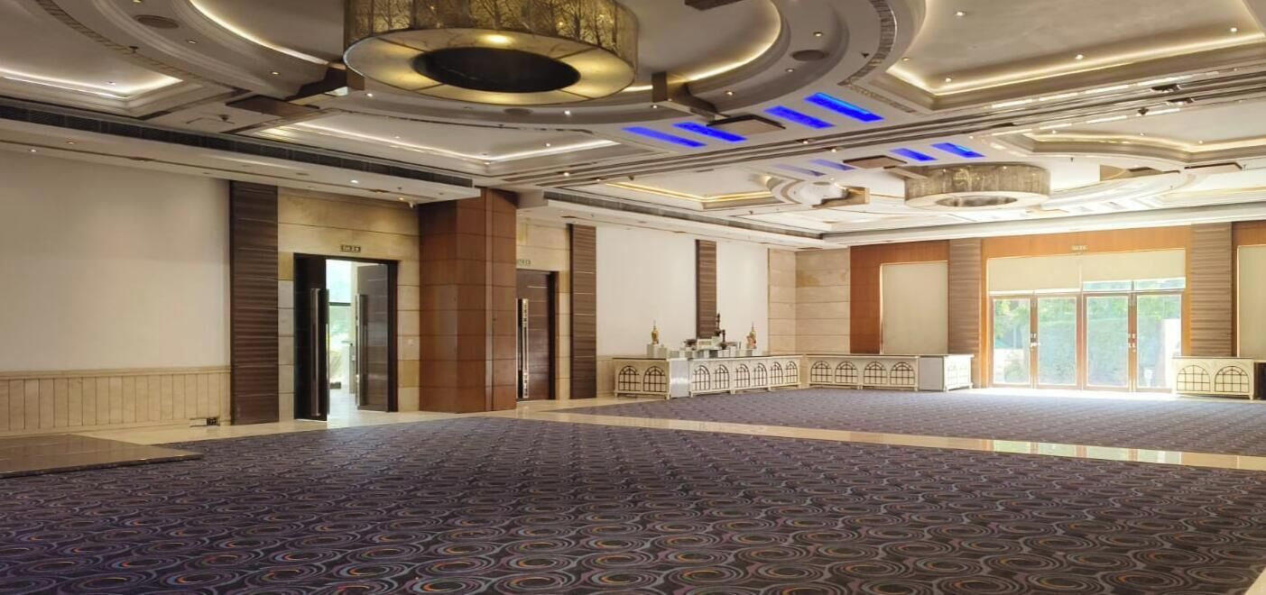 A spacious hall with patterned carpet, a modern ceiling design, and a large window providing natural light.