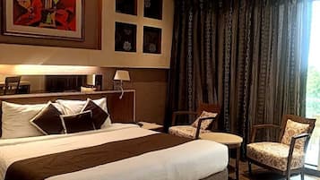 Ein Hotelzimmer mit einem großen Bett, einem Schreibtisch, zwei Stühlen, einem Deckenventilator und einem Bild an der Wand.