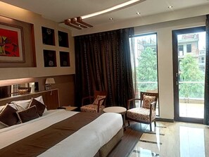 A hotel room with a large bed, two chairs, a small table, and a balcony with a view. - Club Florence (Gurugram)