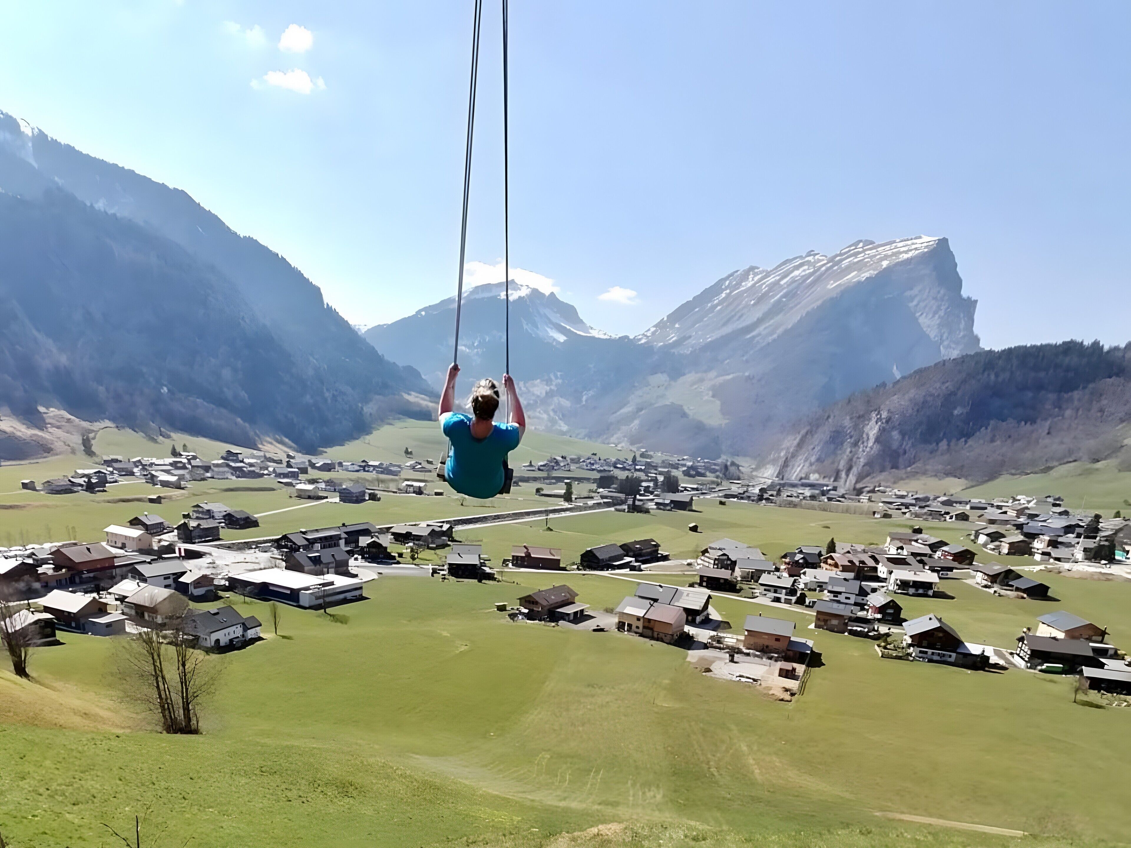 Eine Person schwingt sich in der Luft, im Hintergrund eine gebirgige Landschaft.