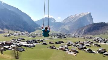 Eine Person schwingt sich in der Luft, im Hintergrund eine gebirgige Landschaft.
