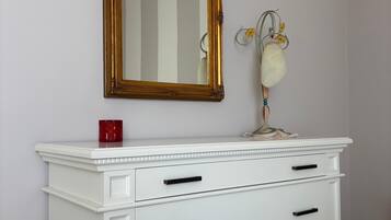 A white dresser with black handles, a gold-framed mirror above it, and a small vase with yellow flowers on the dresser's top.