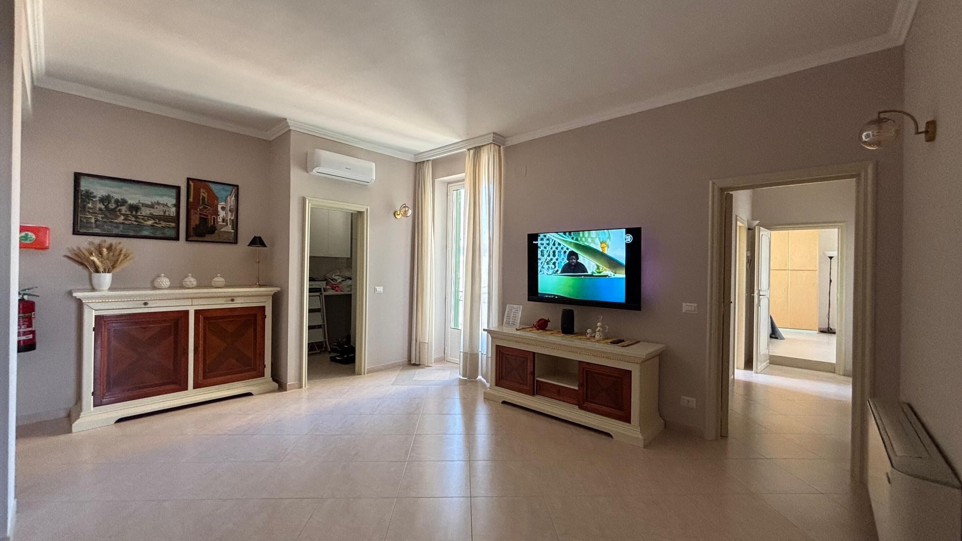 Ein geräumiger Wohnbereich mit Fernseher, Kamin und einem Gang zu einem weiteren Zimmer.