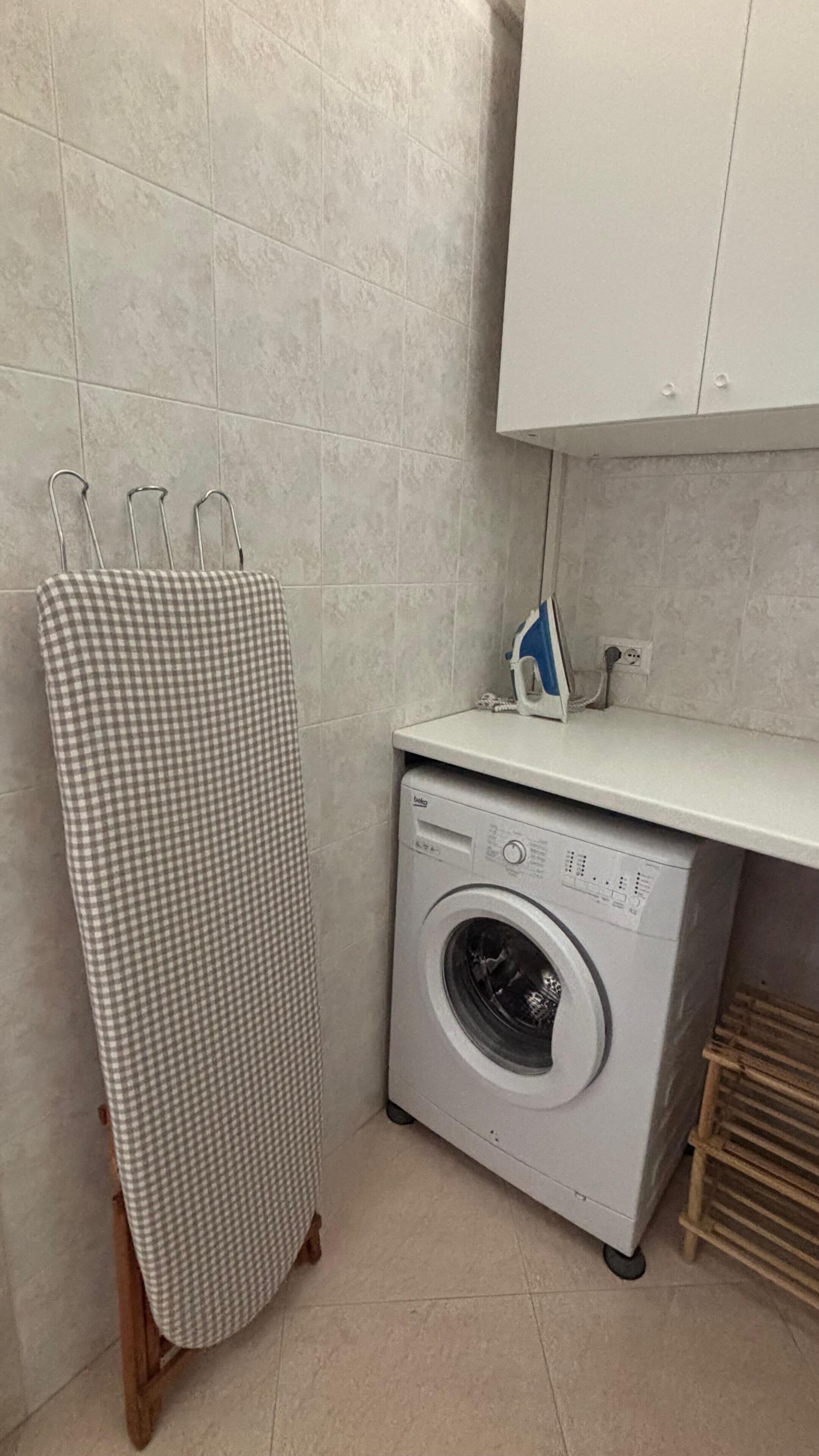 A laundry area with a washing machine, an ironing board, and a drying rack.