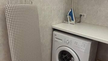 A laundry area with a washing machine, an ironing board, and a drying rack.
