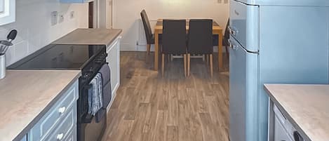 Eine kompakte Küche mit Herd, Backofen und einem blauen Kühlschrank. Ein Esstisch mit Stühlen und ein Bild an der Wand.