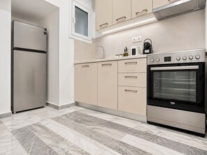 A modern kitchen with a stainless steel refrigerator, a built-in oven, beige cabinets, and a marble-tiled floor. - The Gkyzi Chapter by MPS (Athina)