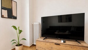 Un salon moderne avec un grand téléviseur à écran plat, un meuble TV en bois, une plante en pot et un radiateur.