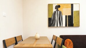 Un coin repas avec une table et des chaises en bois, un vase posé sur la table et un tableau accroché au mur.