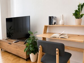 A modern living room with a flat-screen TV, wooden furniture, a potted plant, and books on a shelf. - The Gkyzi Chapter by MPS (Athina)