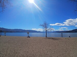 Ein Strand mit blauem Himmel, einem See und Bergen im Hintergrund.