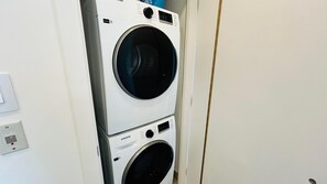 Eine übereinander angeordnete Waschmaschine und ein Trockner mit Bedienfeldern und einem Stromanschluss.