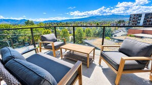 Un balcon aménagé avec du mobilier d’extérieur, une vue sur le paysage urbain et des montagnes à l’horizon.