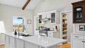 A modern kitchen with white cabinetry, a large island, stainless steel appliances, and a view of the outdoors.