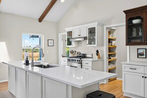 A modern kitchen with white cabinetry, a large island, stainless steel appliances, and a view of the outdoors.