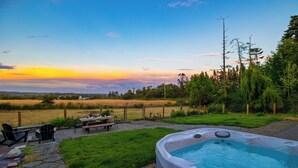 A hot tub in a backyard with a view of the sunset, a picnic table, and chairs.