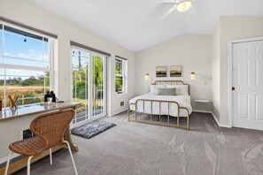 A bedroom with a bed, a desk, and a chair. There are windows and a door.