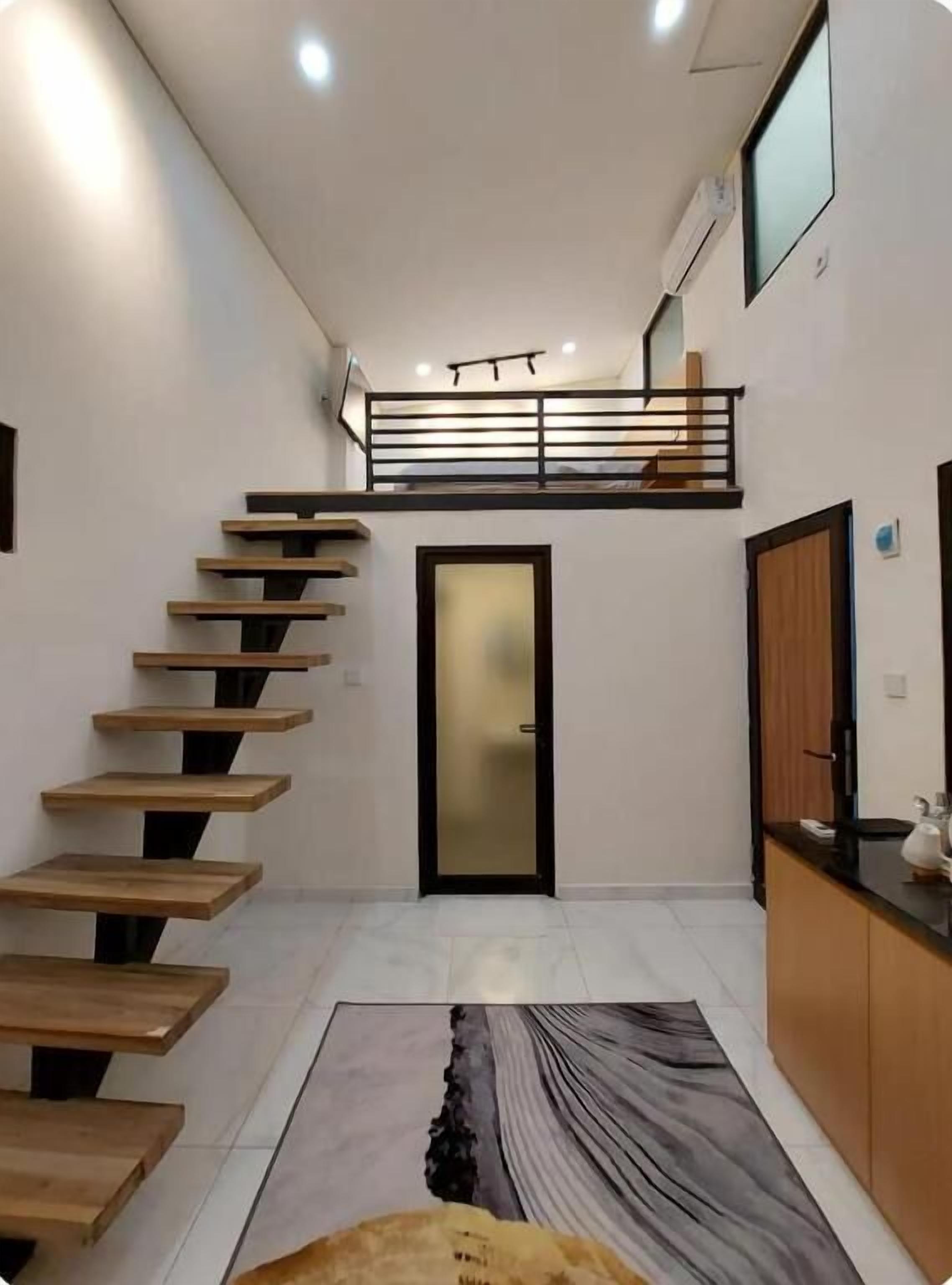 A modern interior with a staircase leading to a loft, a kitchen area, and a door with a frosted glass panel.