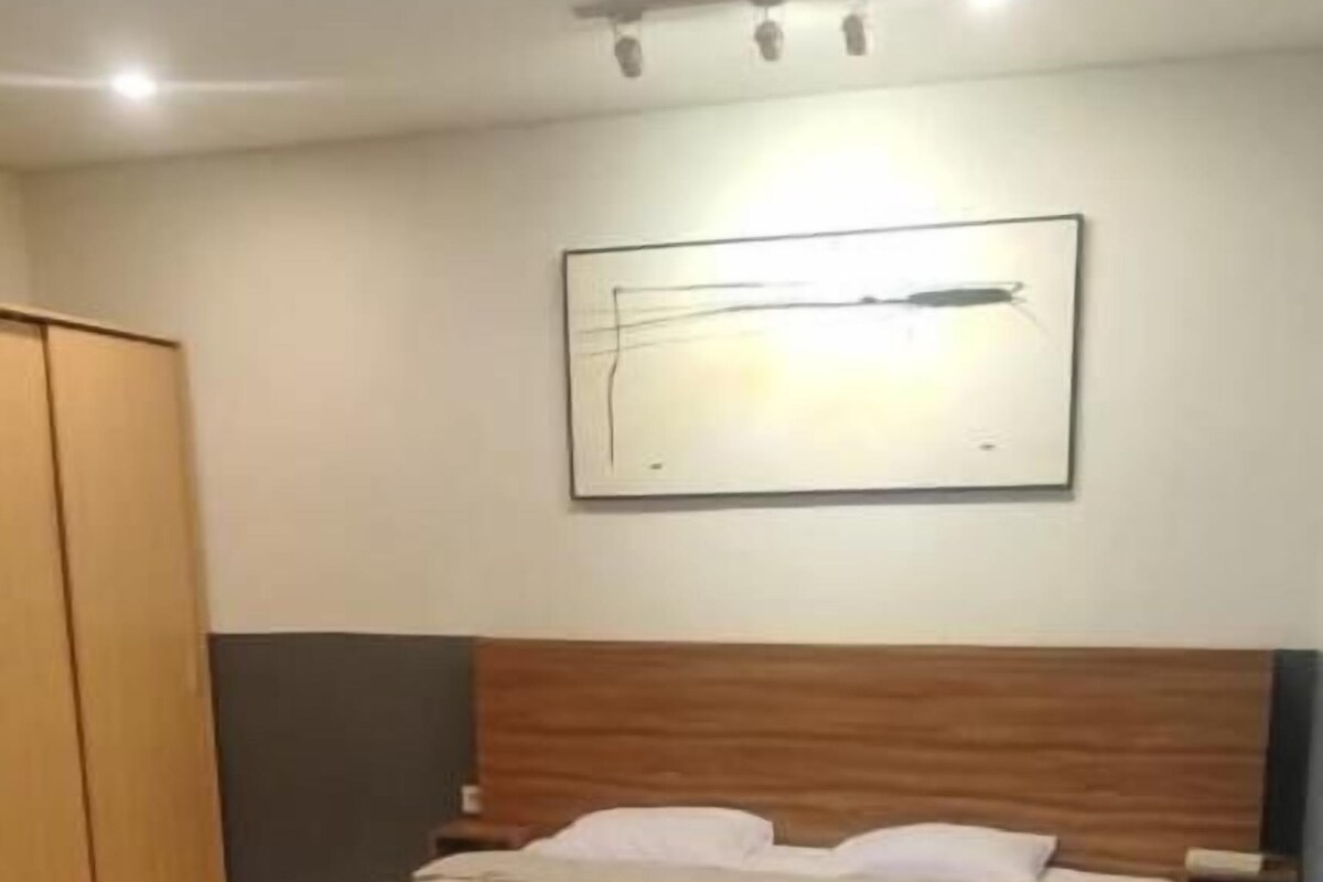 A bedroom with a double bed, a sofa, a wooden headboard, a framed picture on the wall, and a wardrobe.