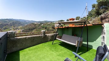 A rooftop terrace with artificial grass, a swing chair, and a view of the surrounding landscape.