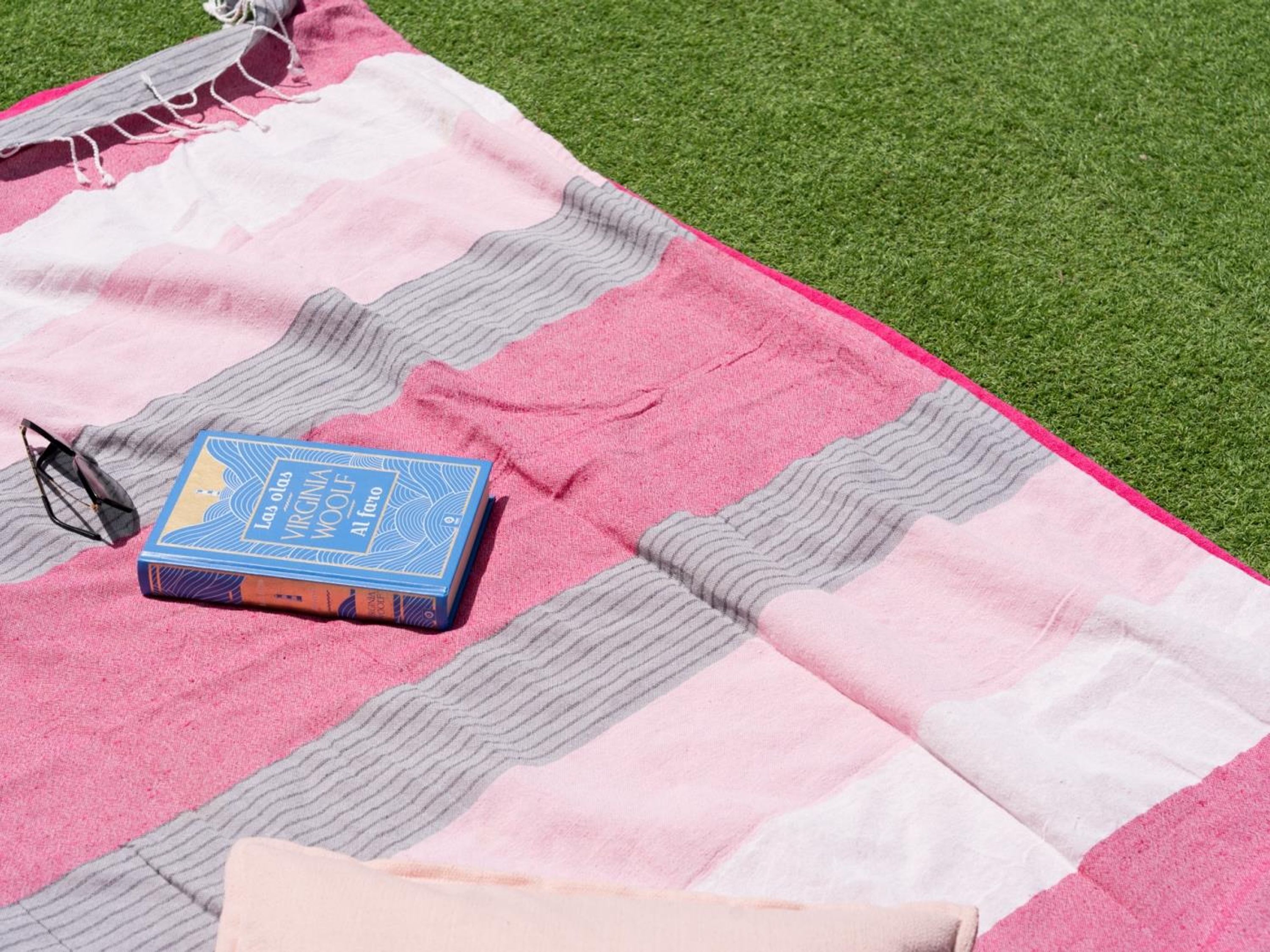 A blanket with a book and sunglasses on a grassy surface.