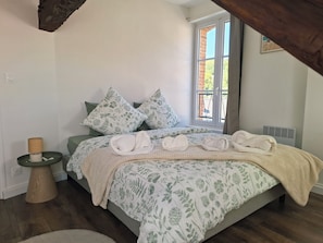 Un dormitorio con cama, almohadas, mesita de noche, lámpara y ventana.