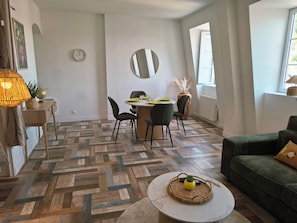 Una sala de estar moderna con suelo de espiga, un comedor con mesa redonda y un sofá verde.