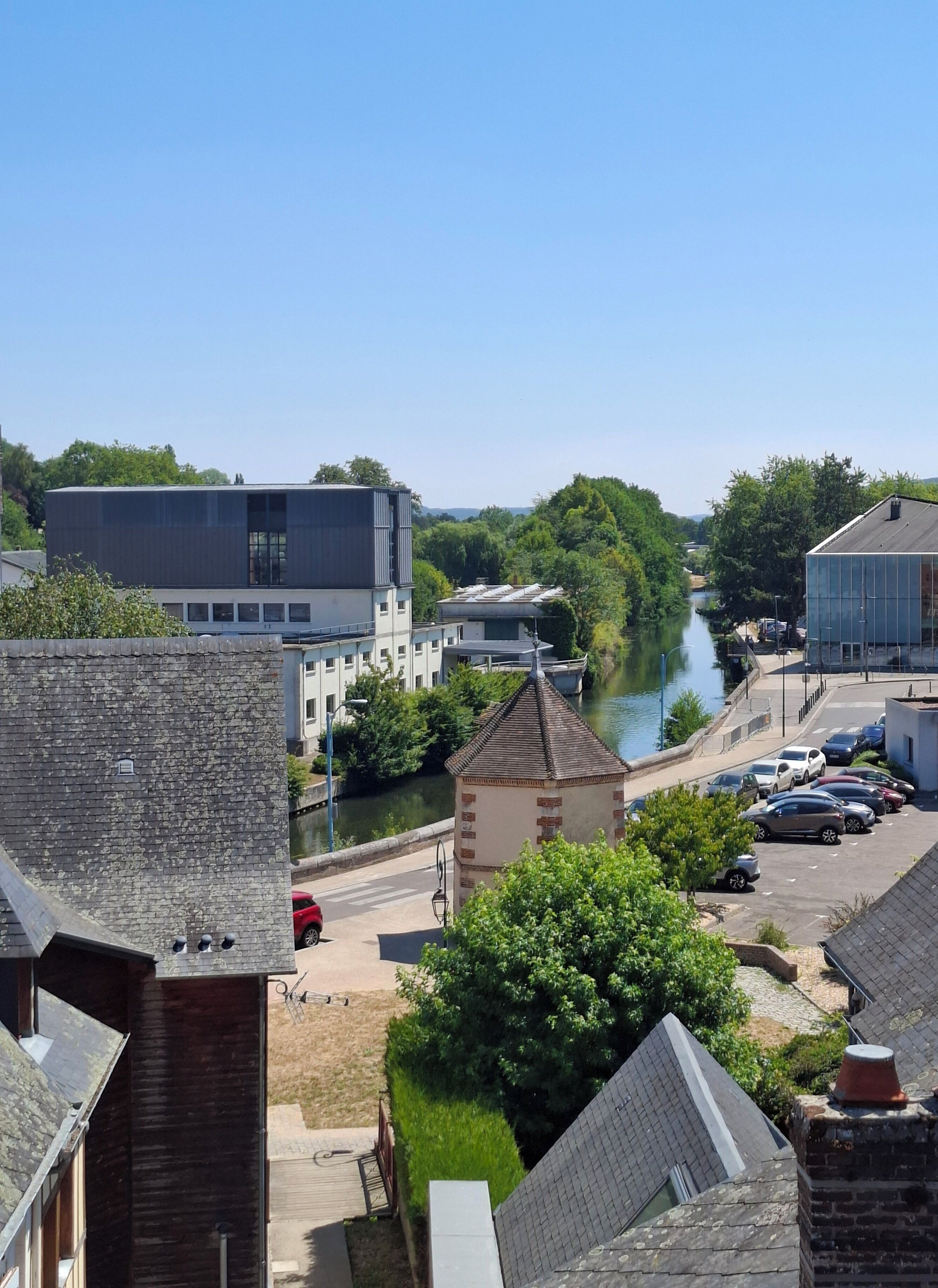A riverside view with modern buildings, a small tower, and parked cars.