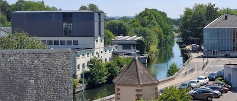 A riverside view with modern buildings, a small tower, and parked cars.
