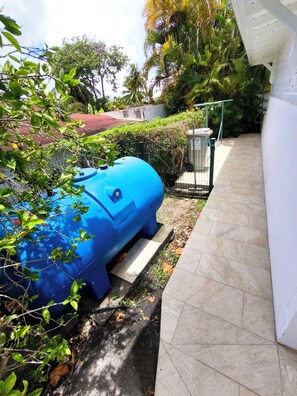 A blue water tank, a white wall, and a tiled pathway.