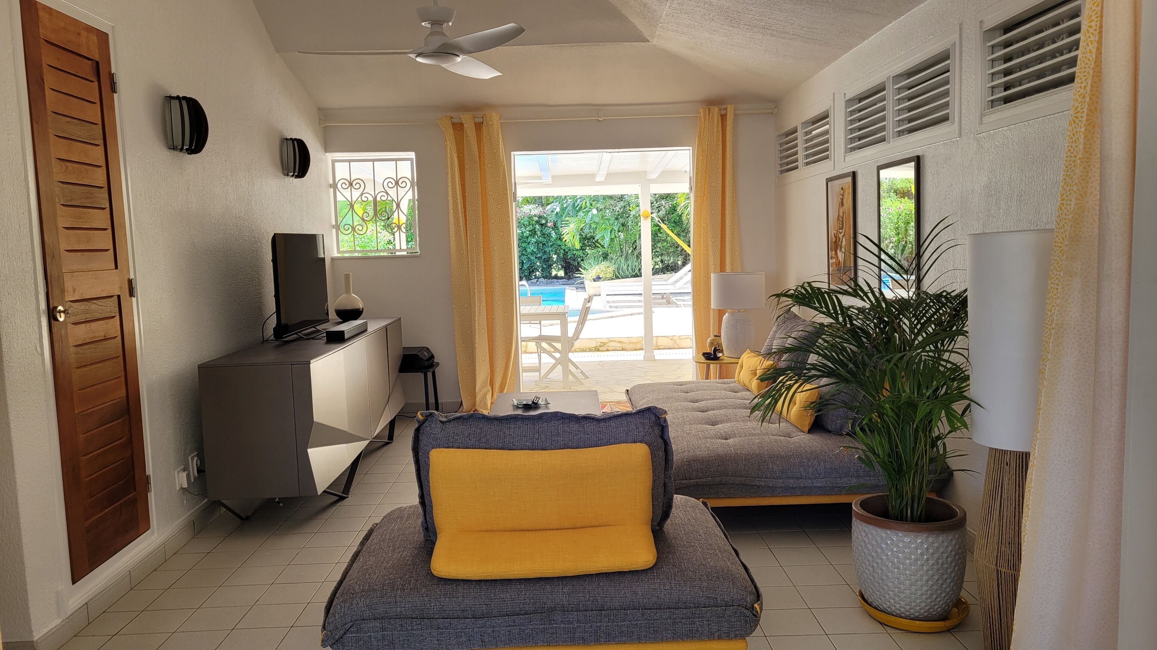 A modern bedroom with a sofa, a TV, a desk, and a view of an outdoor pool area.