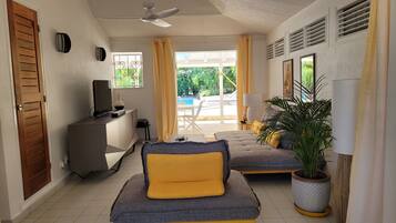 A modern bedroom with a sofa, a TV, a desk, and a view of an outdoor pool area.