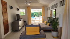 Un dormitorio moderno con sofá, televisor, escritorio y vistas a un área de piscina exterior.