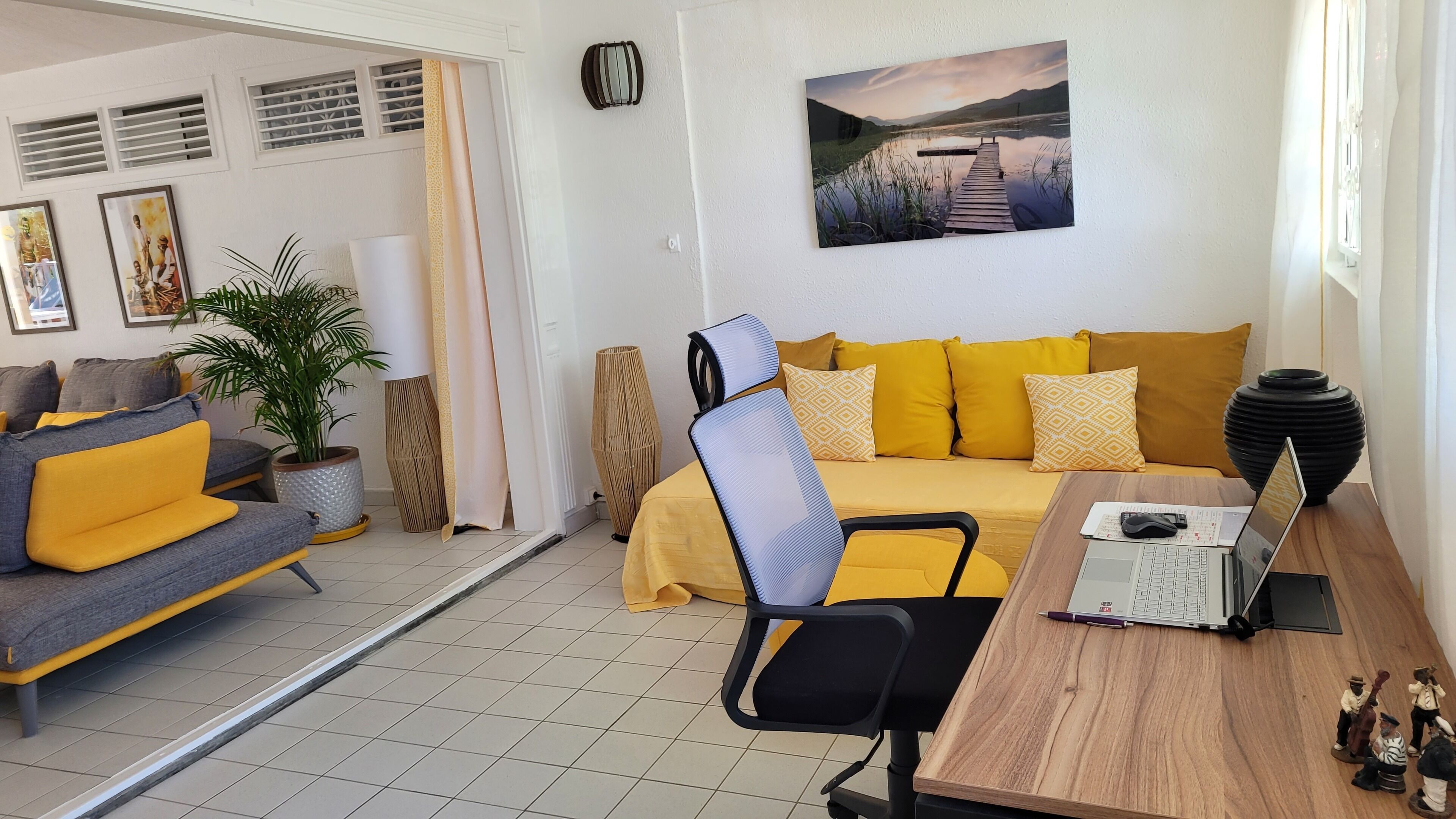 A modern living room with a sofa, a desk with a laptop, a chair, and a large window.