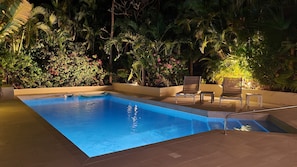 Una piscina con suelo de baldosas, rodeada de abundante vegetación.