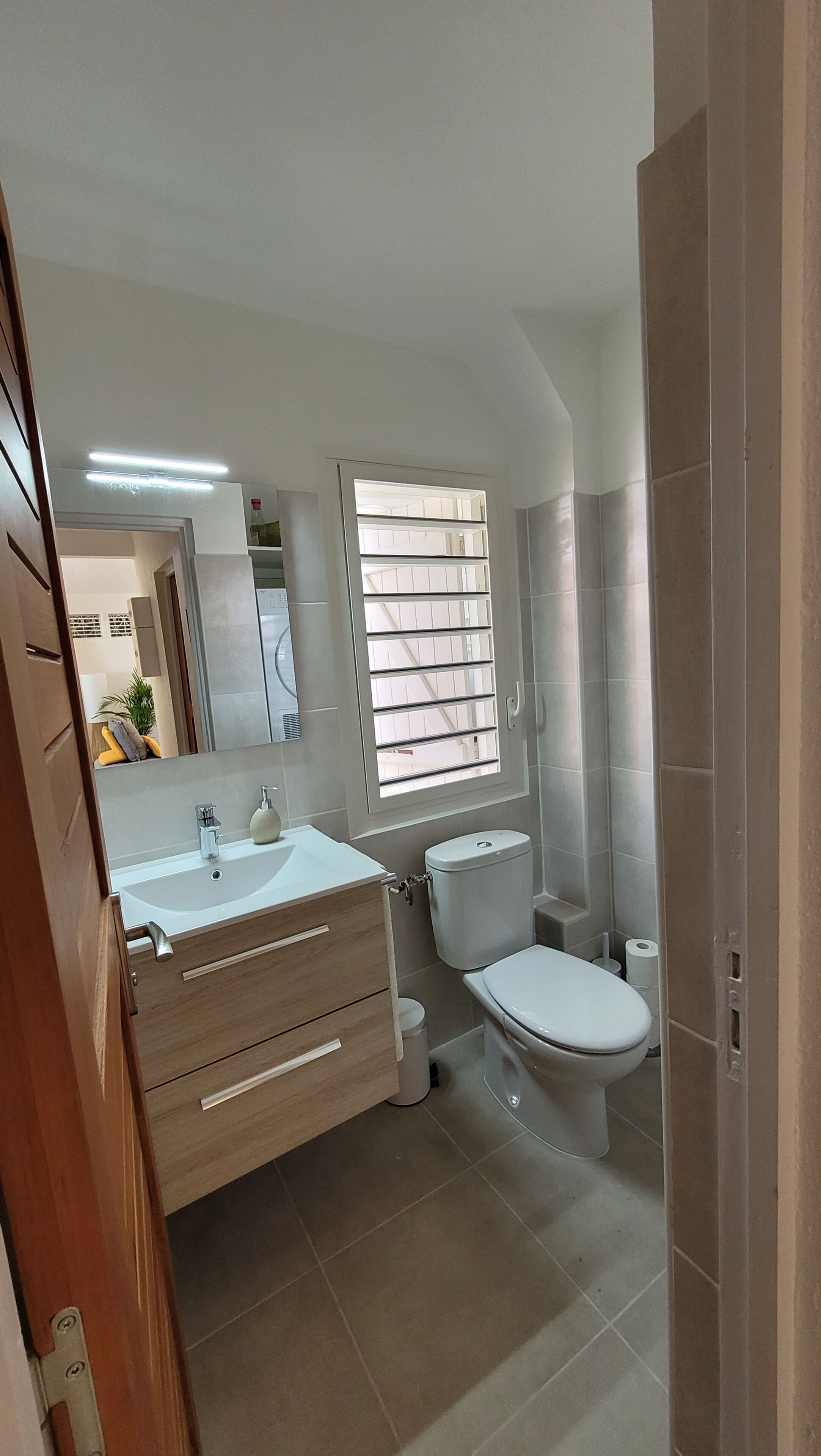 A modern bathroom with a sink, vanity, toilet, and window with blinds.