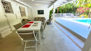 Un patio exterior con mesa y sillas de comedor, piscina y vistas a vegetación exuberante.
