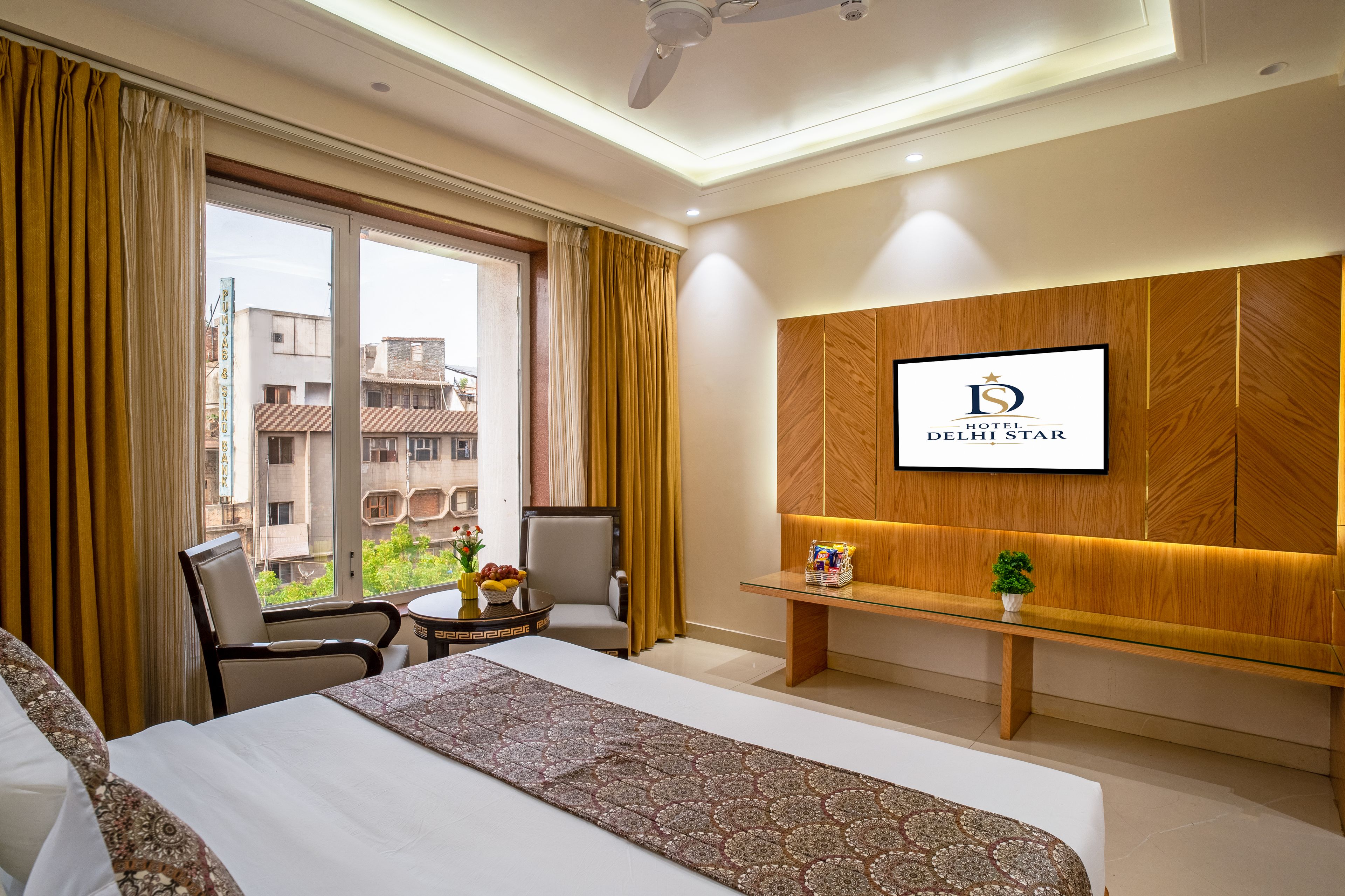 A hotel room with a bed, a desk, a chair, a TV mounted on the wall, and a window with curtains.