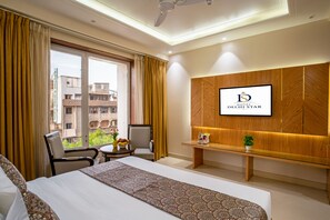 Habitación de hotel con cama, escritorio, silla, televisor montado en la pared y ventana con cortinas.