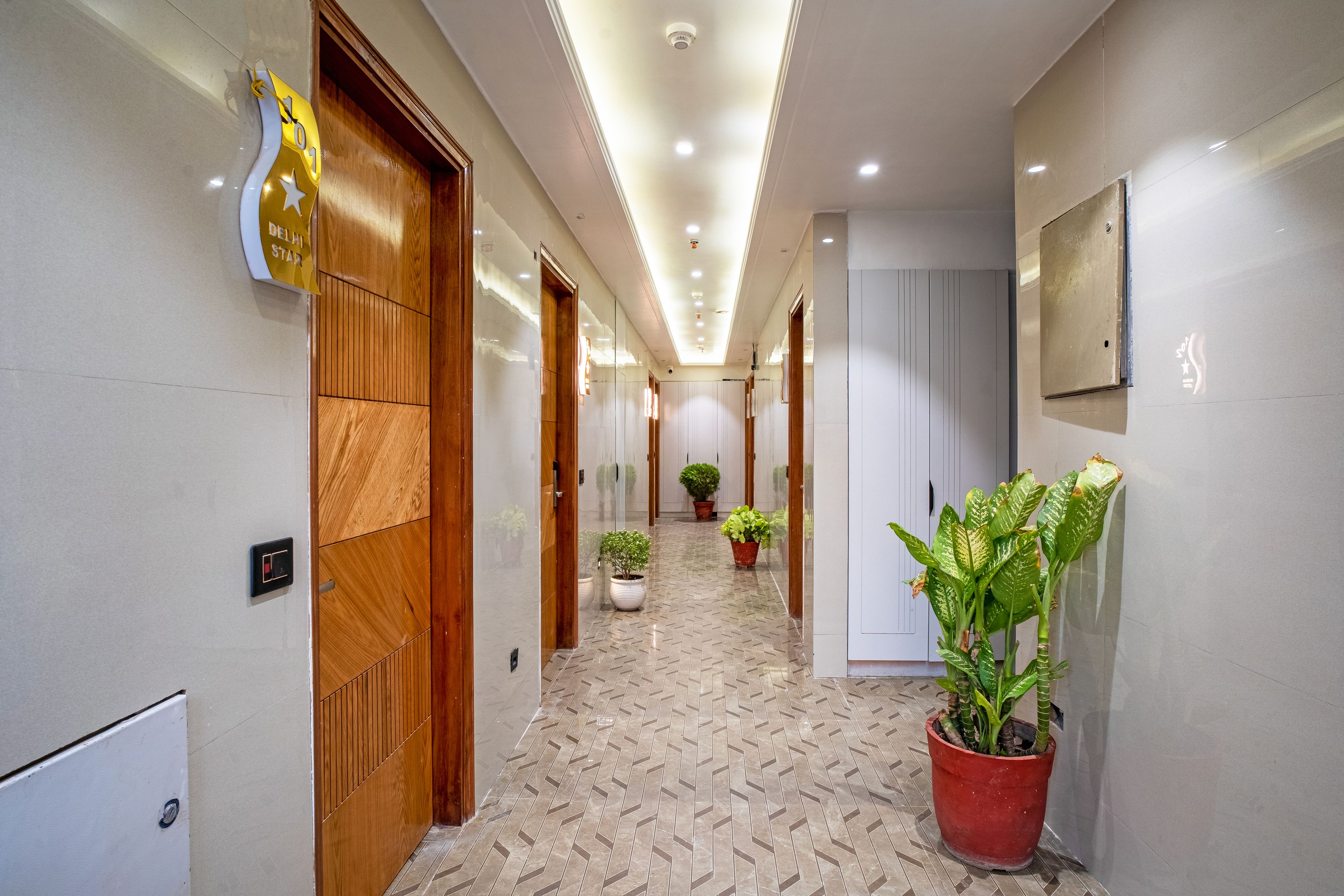 Un pasillo de hotel con puertas de madera, plantas en macetas y piso de baldosas.